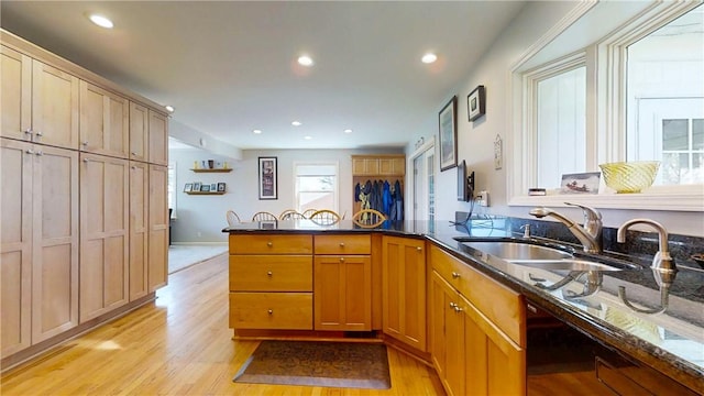 kitchen with recessed lighting, light wood finished floors, dark stone countertops, a sink, and a peninsula