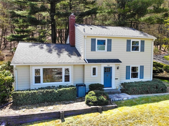 traditional-style home with a chimney, a front lawn, roof with shingles, and central air condition unit