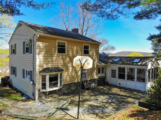 rear view of property featuring a chimney, a sunroom, a patio, and a shingled roof