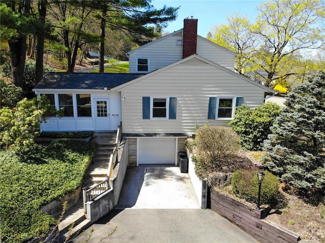 view of front of property featuring roof with shingles, a chimney, concrete driveway, an attached garage, and stairs