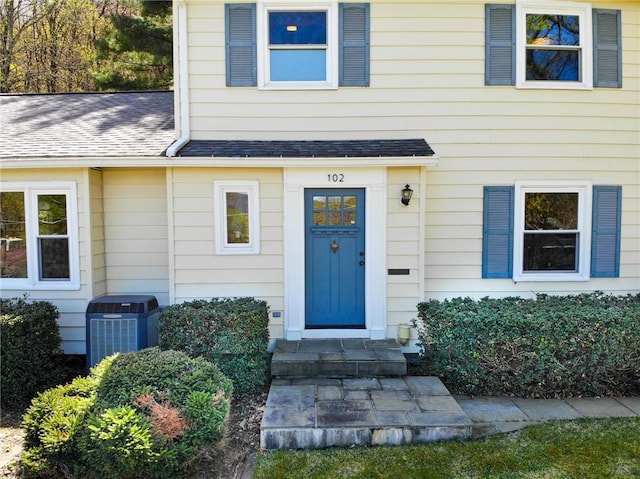 doorway to property with roof with shingles and central AC