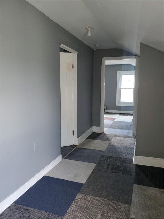 corridor featuring vaulted ceiling, baseboards, and carpet