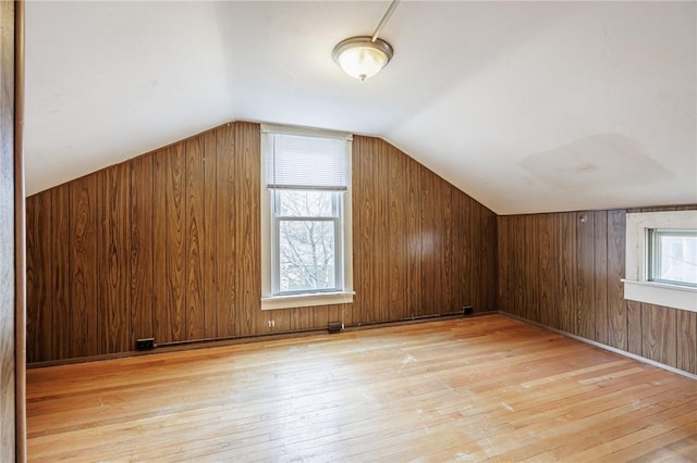 additional living space featuring light wood-style flooring, wood walls, and vaulted ceiling