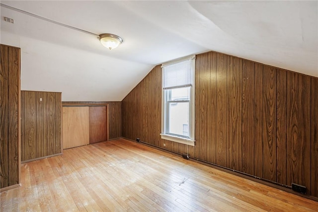 additional living space featuring vaulted ceiling, light wood-type flooring, visible vents, and wooden walls