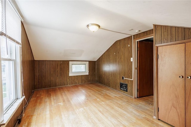 bonus room with light wood-type flooring, vaulted ceiling, and wood walls
