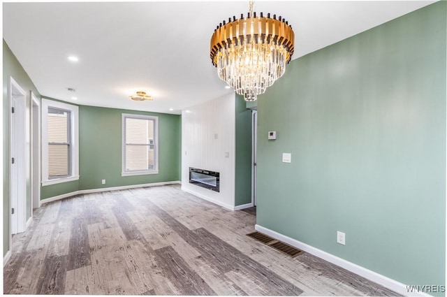 unfurnished living room featuring baseboards, wood finished floors, visible vents, and a chandelier