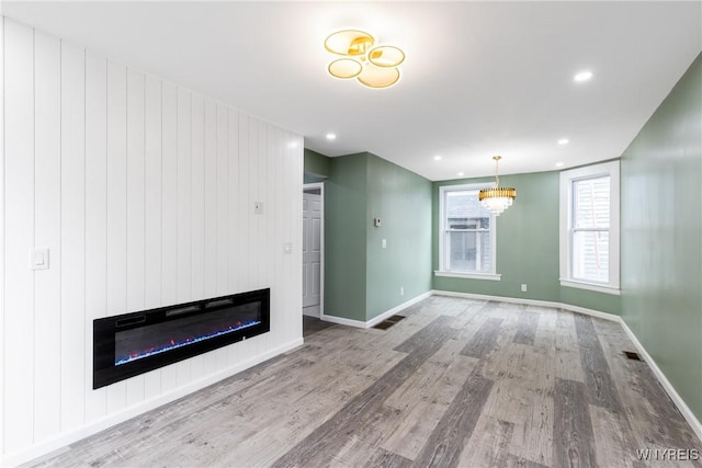 unfurnished living room featuring baseboards, a glass covered fireplace, wood finished floors, and recessed lighting