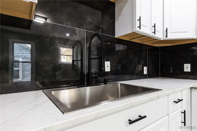 kitchen with light stone countertops, white cabinetry, decorative backsplash, and a sink