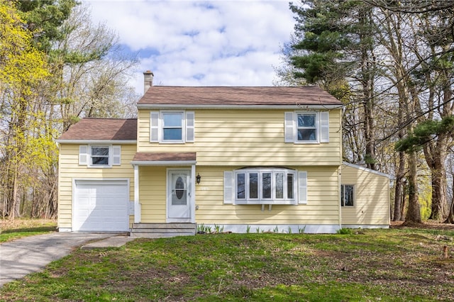 colonial home with an attached garage, driveway, a chimney, and a front yard