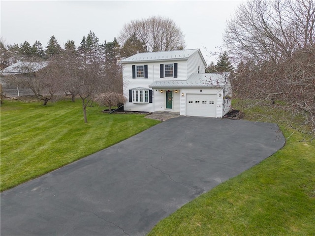 traditional-style home with an attached garage, aphalt driveway, a front yard, and metal roof