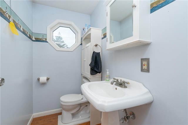 bathroom featuring baseboards, wood finished floors, and toilet