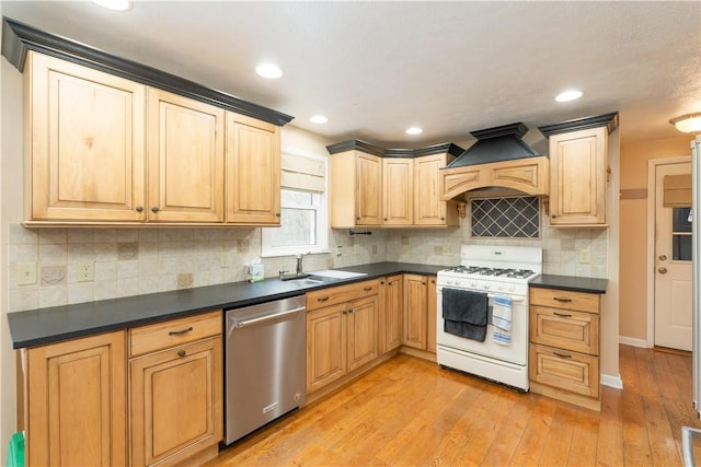 kitchen featuring dark countertops, a sink, dishwasher, premium range hood, and gas range gas stove