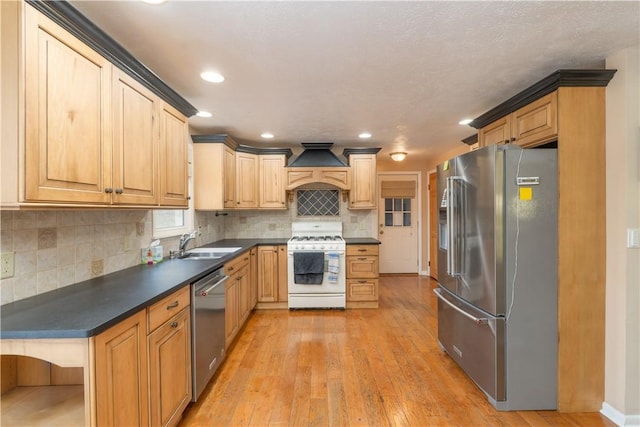 kitchen with dark countertops, a sink, premium range hood, light wood-style flooring, and appliances with stainless steel finishes