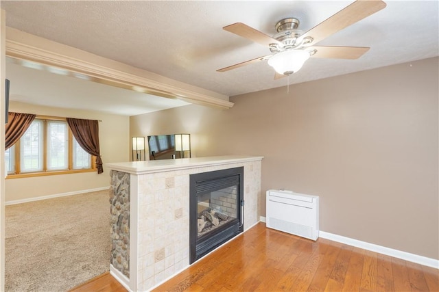 interior space featuring a glass covered fireplace, wood finished floors, baseboards, and ceiling fan
