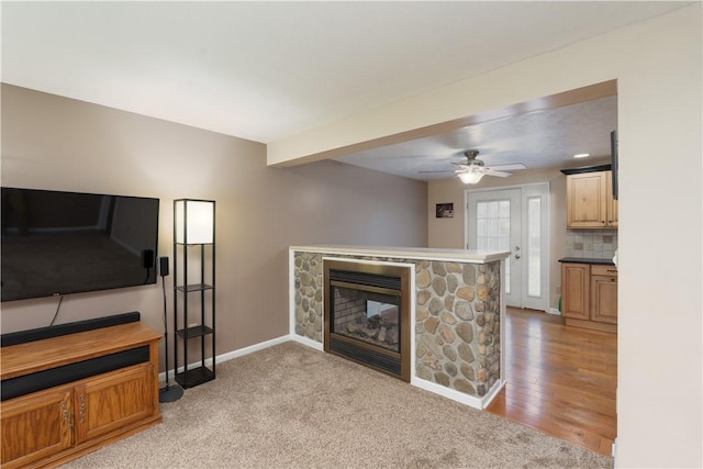 living room featuring a fireplace, light carpet, baseboards, and ceiling fan