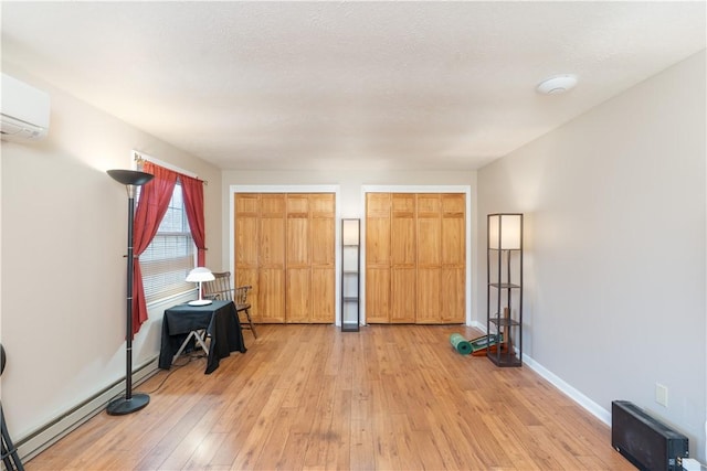 unfurnished bedroom featuring a baseboard radiator, light wood-type flooring, baseboards, and a wall unit AC