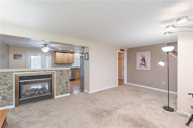 unfurnished living room with a fireplace, a ceiling fan, baseboards, and light carpet