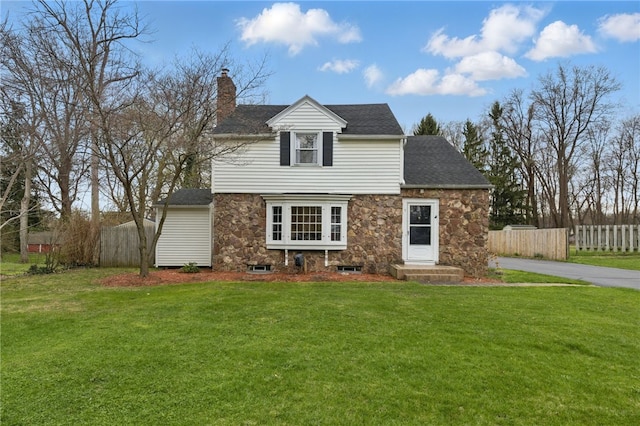 view of front of property featuring roof with shingles, a front lawn, stone siding, a chimney, and fence