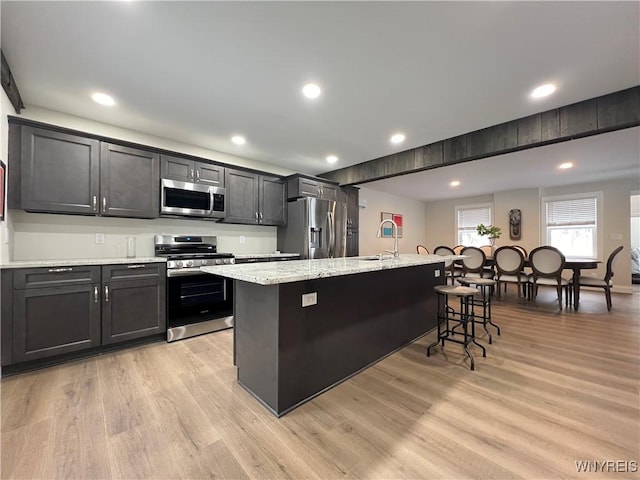 kitchen featuring a kitchen bar, light wood-style flooring, a center island with sink, and stainless steel appliances