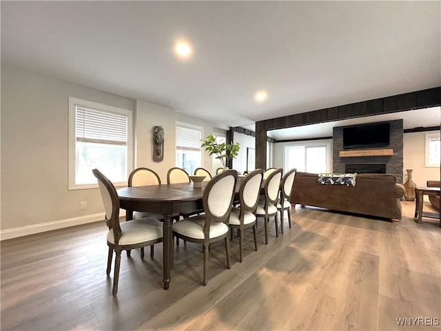 dining space with a large fireplace, baseboards, wood finished floors, and a wealth of natural light