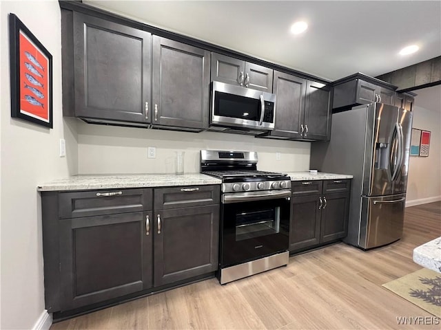 kitchen with recessed lighting, light stone counters, light wood-style floors, baseboards, and appliances with stainless steel finishes
