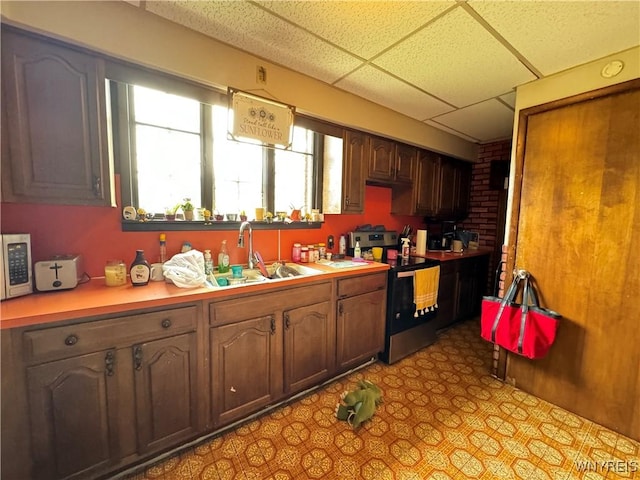 kitchen featuring a drop ceiling, light floors, light countertops, a sink, and stainless steel electric range oven