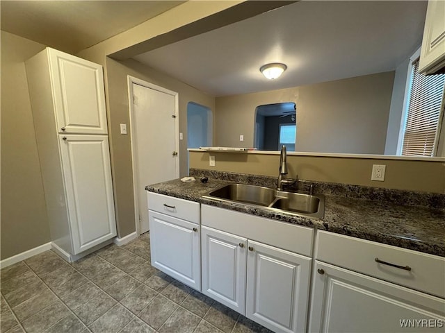 kitchen with dark countertops, a sink, arched walkways, white cabinets, and baseboards