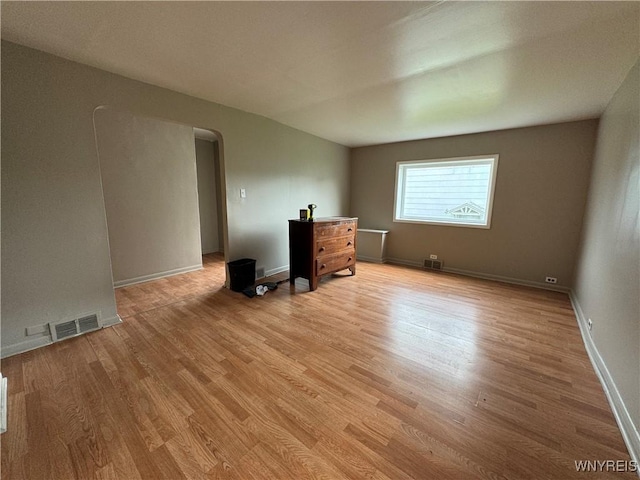 unfurnished room with baseboards, arched walkways, visible vents, and light wood-type flooring