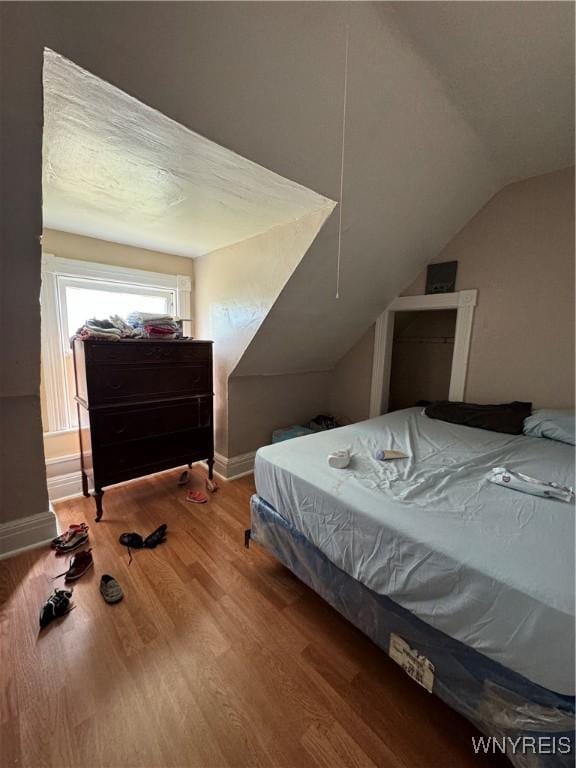 bedroom featuring lofted ceiling, baseboards, and wood finished floors