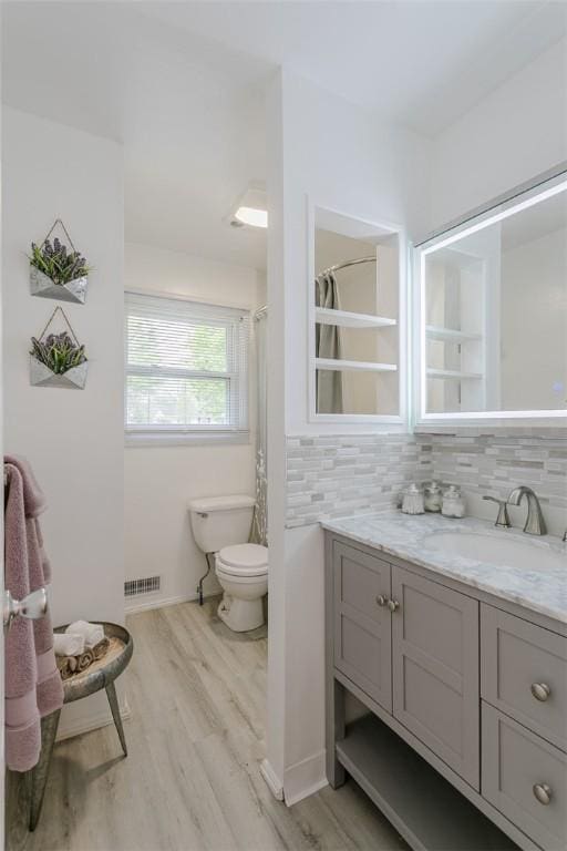 full bathroom with toilet, visible vents, backsplash, wood finished floors, and vanity