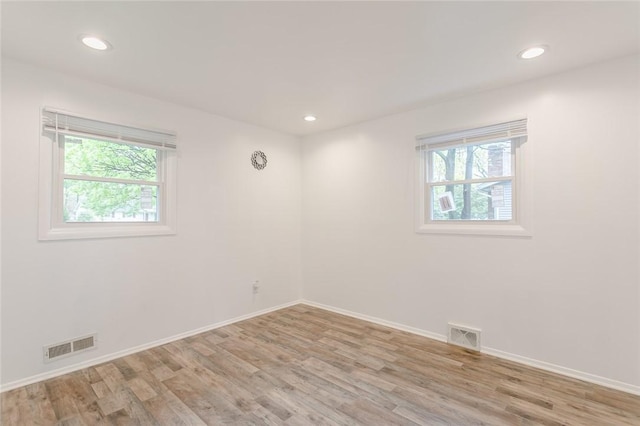 empty room featuring light wood-style flooring, visible vents, and a wealth of natural light