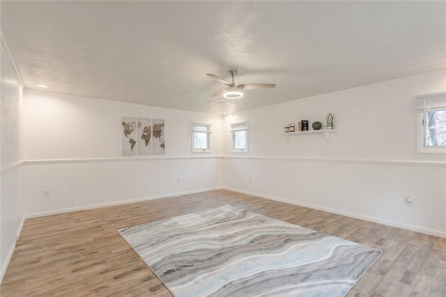 empty room featuring wainscoting, a ceiling fan, wood finished floors, and a wealth of natural light