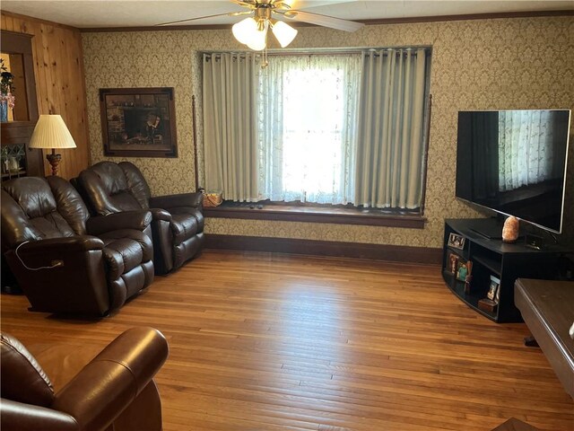 living area with ceiling fan, baseboards, ornamental molding, and wallpapered walls