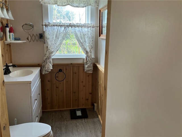 bathroom featuring a wainscoted wall, wooden walls, wood finished floors, toilet, and vanity