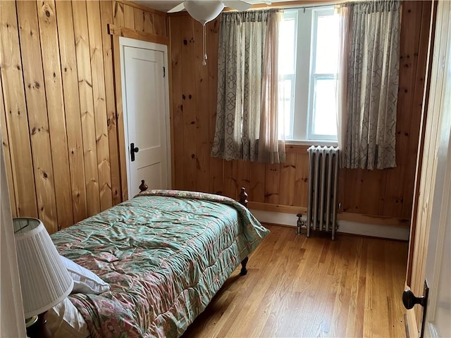 bedroom featuring radiator, wood walls, and light wood-type flooring