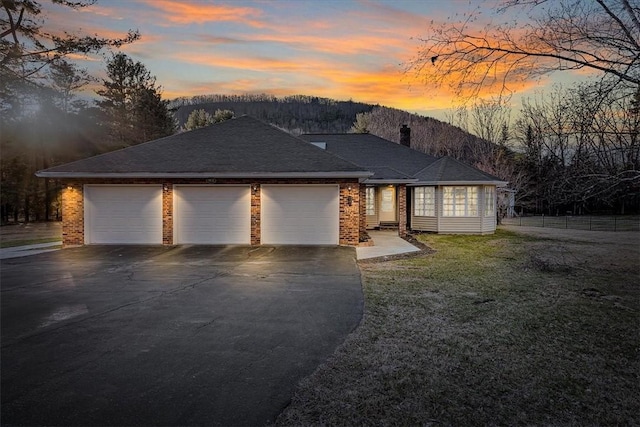 ranch-style home with aphalt driveway, fence, a lawn, brick siding, and a garage