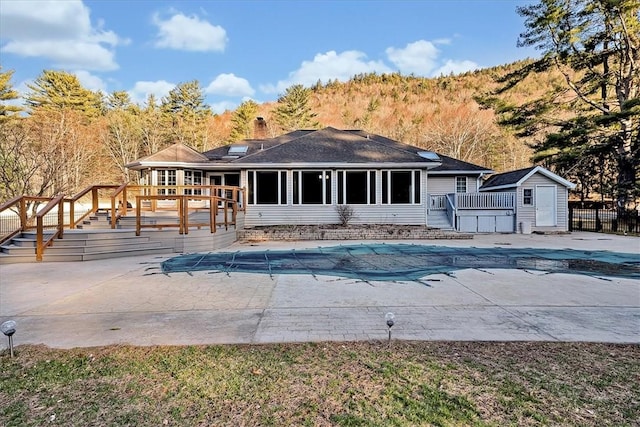 rear view of house featuring a fenced in pool, stairs, a wooden deck, an outbuilding, and a sunroom