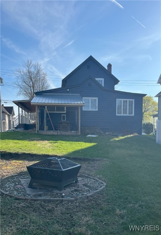 back of house featuring a lawn, a chimney, and an outdoor fire pit