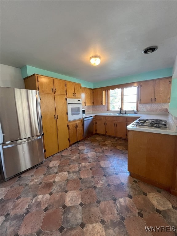 kitchen featuring light countertops, a sink, brown cabinets, and appliances with stainless steel finishes