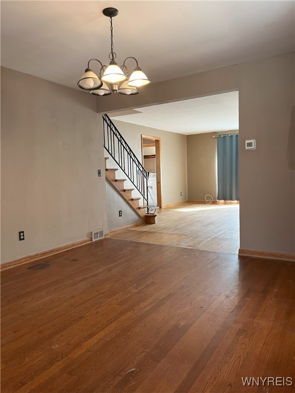 unfurnished living room featuring stairway, an inviting chandelier, wood finished floors, visible vents, and baseboards