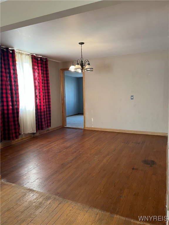 empty room with baseboards, hardwood / wood-style flooring, and a notable chandelier