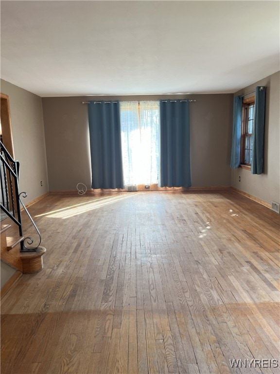 unfurnished living room featuring baseboards, stairs, hardwood / wood-style floors, and plenty of natural light