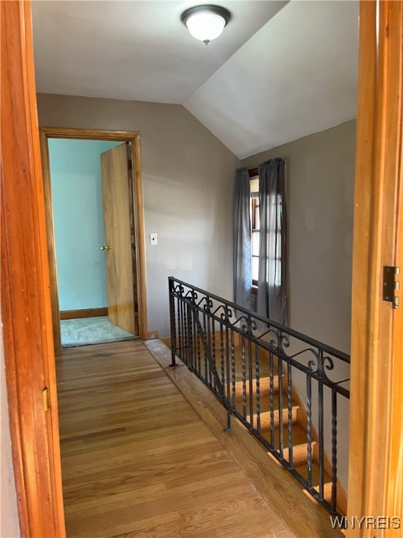 corridor featuring vaulted ceiling, wood finished floors, an upstairs landing, and baseboards