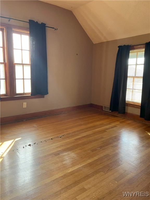 additional living space featuring wood-type flooring, vaulted ceiling, visible vents, and baseboards