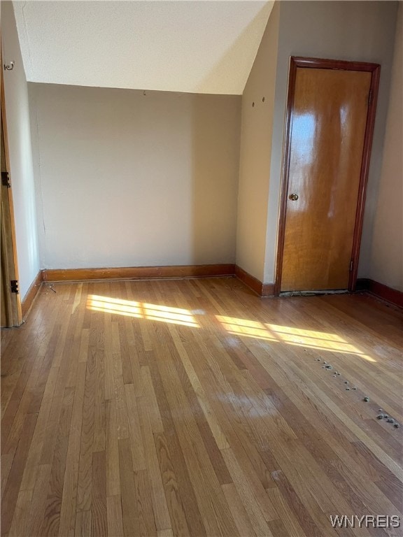 additional living space featuring wood finished floors, lofted ceiling, and baseboards