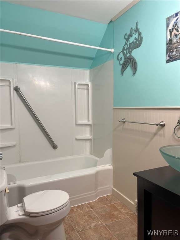 bathroom with toilet, shower / bathing tub combination, wainscoting, stone finish floor, and vanity