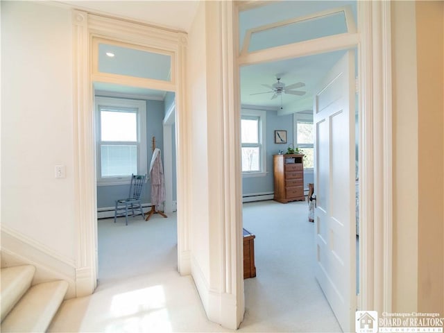 hall featuring a baseboard heating unit, a healthy amount of sunlight, and light colored carpet