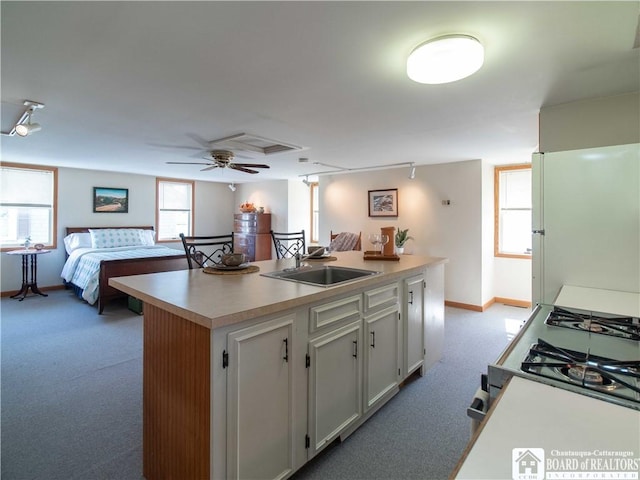 kitchen with white cabinets, light carpet, a sink, freestanding refrigerator, and baseboards