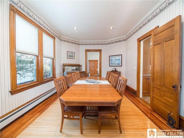 dining room featuring a baseboard heating unit, wallpapered walls, light wood finished floors, and ornamental molding