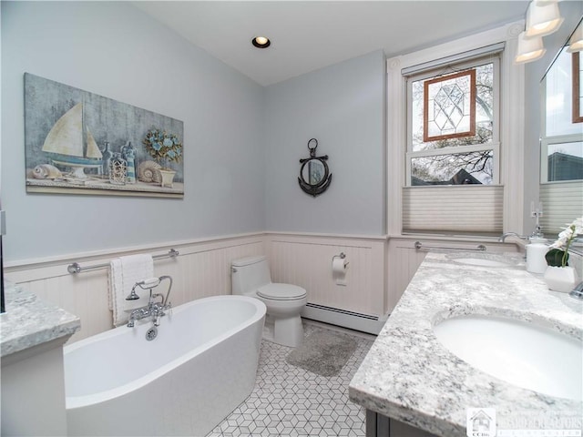 bathroom with double vanity, a sink, a baseboard heating unit, wainscoting, and a soaking tub